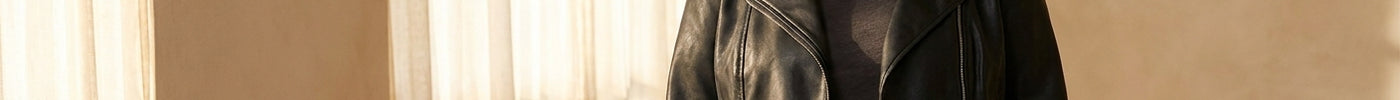 A woman wearing a fitted black faux leather jacket posed in soft natural light against a neutral background, exuding confident and approachable style.